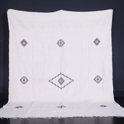 Moroccan man holding or standing near a white 6.2 x 9.2 FT flat woven Berber kilim rug