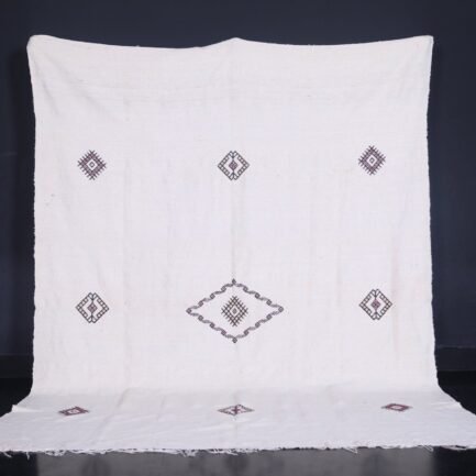 Moroccan man holding or standing near a white 6.2 x 9.2 FT flat woven Berber kilim rug