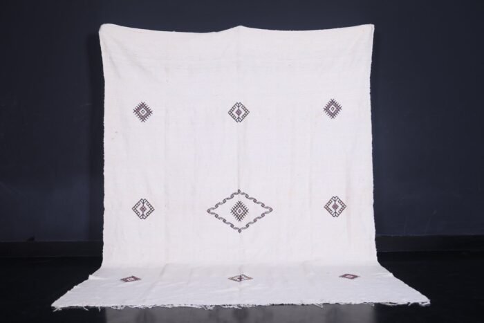 Moroccan man holding or standing near a white 6.2 x 9.2 FT flat woven Berber kilim rug