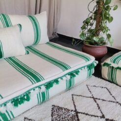 Left side of Moroccan wool couch in cream with green stripes and pom-pom edges – playful handcrafted floor seating