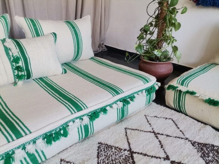 Left side of Moroccan wool couch in cream with green stripes and pom-pom edges – playful handcrafted floor seating