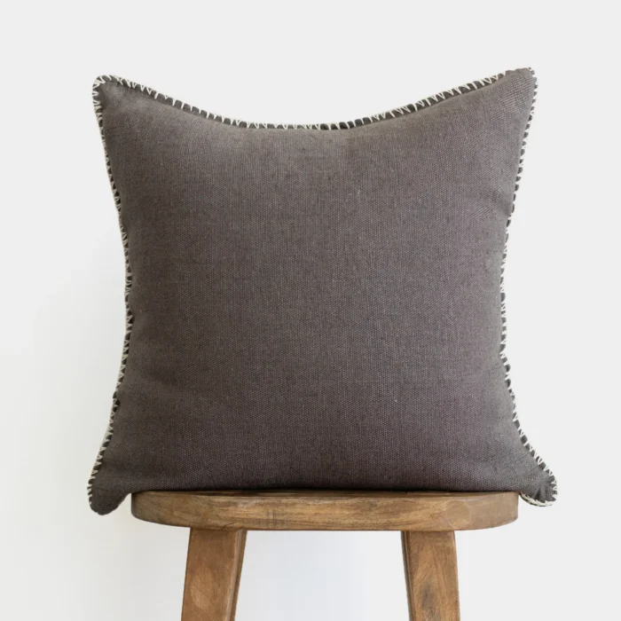 Dark charcoal Moroccan pillow with visible hand-stitched edges – handmade cotton cushion cover on rustic wooden stool, minimalist boho home decor