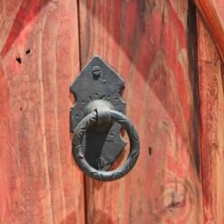 Detail of traditional black iron door knocker on carved red Moroccan wood panel