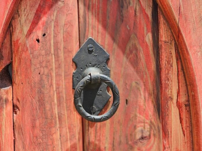 Detail of traditional black iron door knocker on carved red Moroccan wood panel