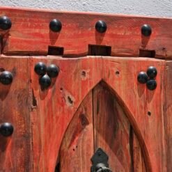 Upper section of red Moroccan wood panel showing iron studs and arched construction
