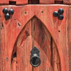 Rustic Moroccan panel featuring arched design with centered iron knocker on red wood