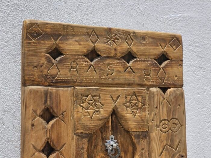 Upper part of handcrafted Moroccan wooden panel featuring geometric Berber carvings and rustic wood finish