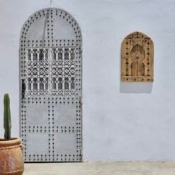 Moroccan panel mounted on white wall next to arched traditional door and cactus