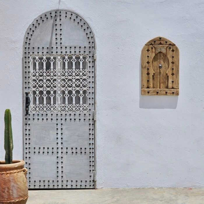 Moroccan panel mounted on white wall next to arched traditional door and cactus