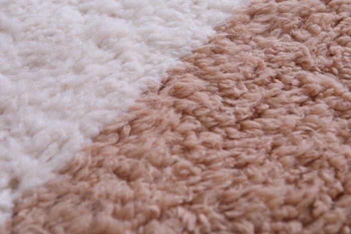 Macro zoom of wool texture on ivory and tan Moroccan rug, displaying natural fiber detail and luxurious density.