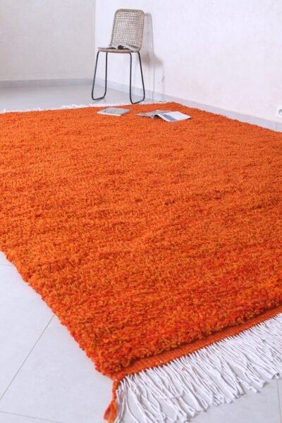 handmade Moroccan wool rug in vibrant rustic orange, featuring authentic Berber tribal designs, natural lamb’s wool material, and finished with traditional fringed tassels.
