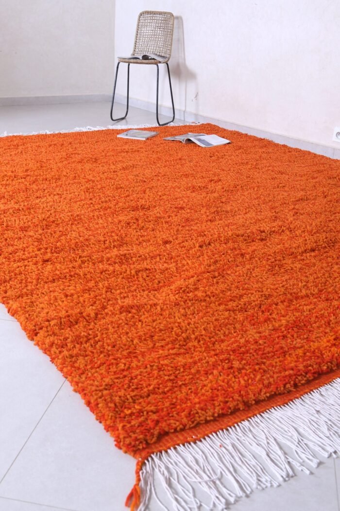 handmade Moroccan wool rug in vibrant rustic orange, featuring authentic Berber tribal designs, natural lamb’s wool material, and finished with traditional fringed tassels.