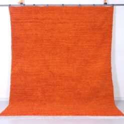 Right side view of a vibrant orange Moroccan wool rug, hand-knotted with traditional Berber Beni Ourain tribal designs, showcasing soft natural lamb’s wool texture and warm rustic hues.