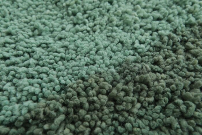 Macro close-up showing the soft, dense texture of natural lamb wool used in the Moroccan green and pistachio rug.