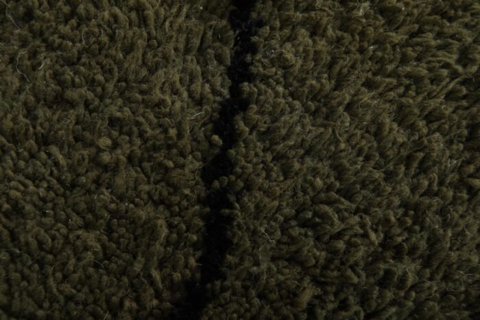 Macro shot highlighting dense lamb wool fibers and rich texture of dark green and black handmade Moroccan rug.