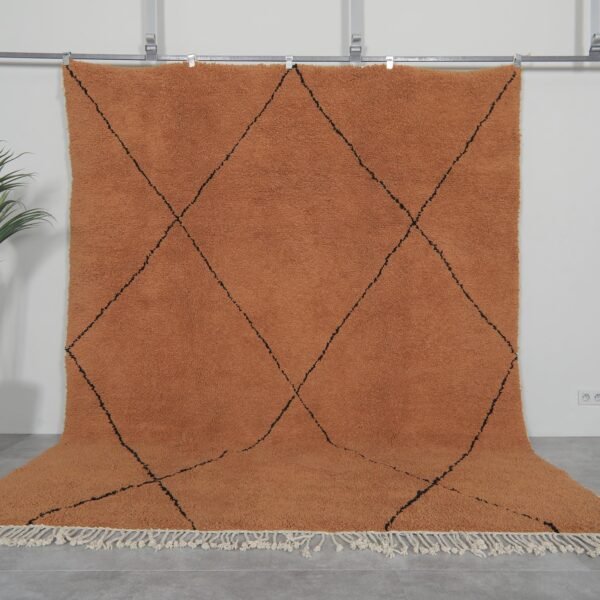 Handmade Moroccan rug with rust base color and black trellis pattern, crafted from 100% natural lamb wool by Berber artisans using traditional Beni Ourain weaving techniques.
