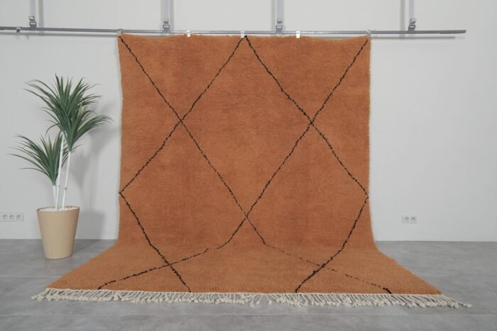 Handmade Moroccan rug with rust base color and black trellis pattern, crafted from 100% natural lamb wool by Berber artisans using traditional Beni Ourain weaving techniques.