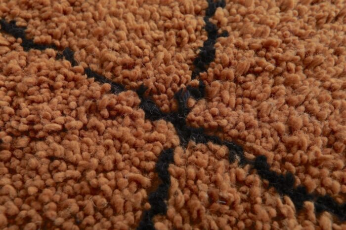 Macro shot highlighting dense lamb wool fibers and rich texture of rust and black handmade Moroccan rug.