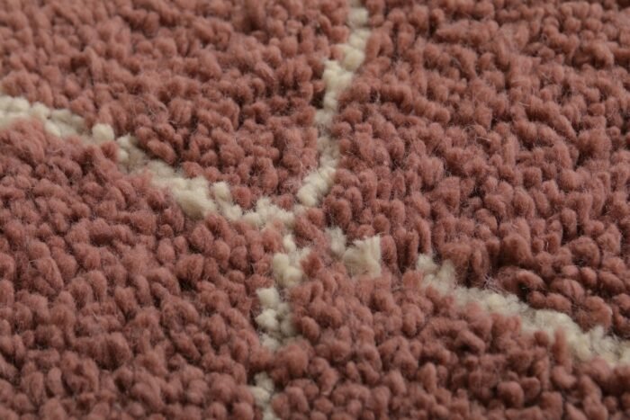 Macro shot of plush lamb wool texture in a handmade chestnut Moroccan rug with ivory trellis, showing the warmth and softness of the material.