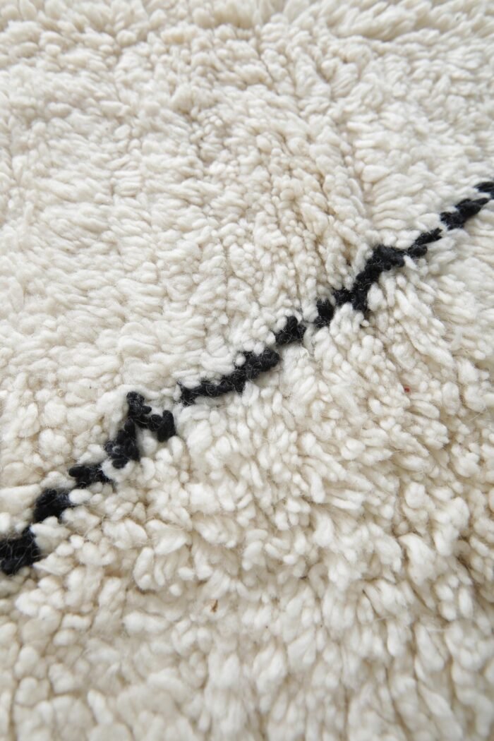 Macro shot highlighting dense lamb wool fibers and rich texture of ivory and black Moroccan hand-knotted rug.
