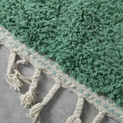 fringe on forest green and aqua Moroccan rug, highlighting handmade wool finish.