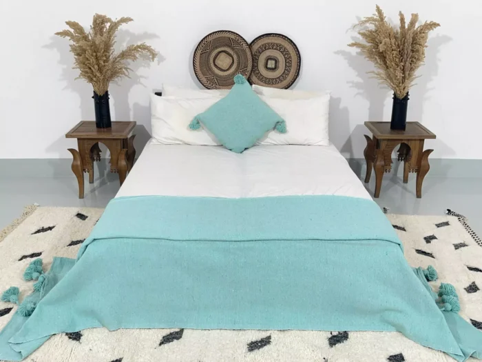Moroccan turquoise pompom throw styled on a cozy bed