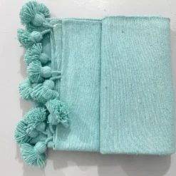 Turquoise Moroccan cotton pompom blanket draped on a sofa