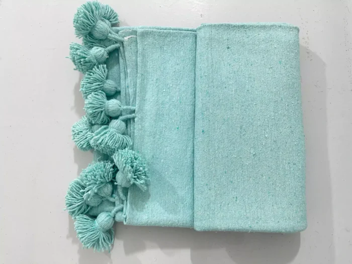 Turquoise Moroccan cotton pompom blanket draped on a sofa