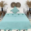 Handmade Moroccan pompom blanket in solid turquoise color on bed