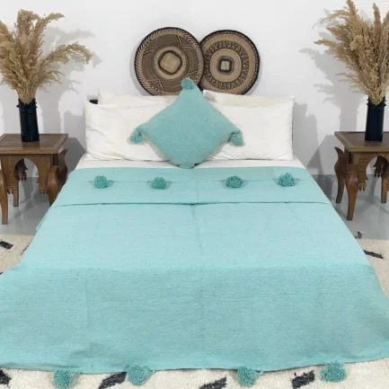 Handmade Moroccan pompom blanket in solid turquoise color on bed