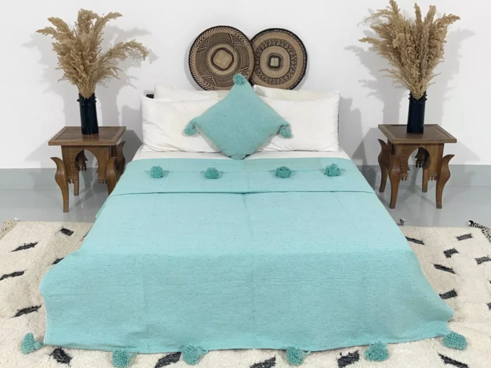 Handmade Moroccan pompom blanket in solid turquoise color on bed