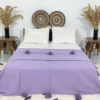 Handmade Moroccan pompom blanket in solid purple displayed on a bed