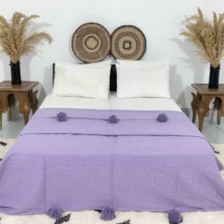 Handmade Moroccan pompom blanket in solid purple displayed on a bed