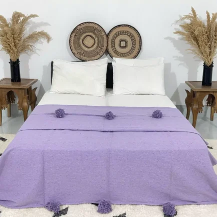 Handmade Moroccan pompom blanket in solid purple displayed on a bed