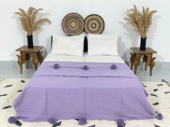 Handmade Moroccan pompom blanket in solid purple displayed on a bed
