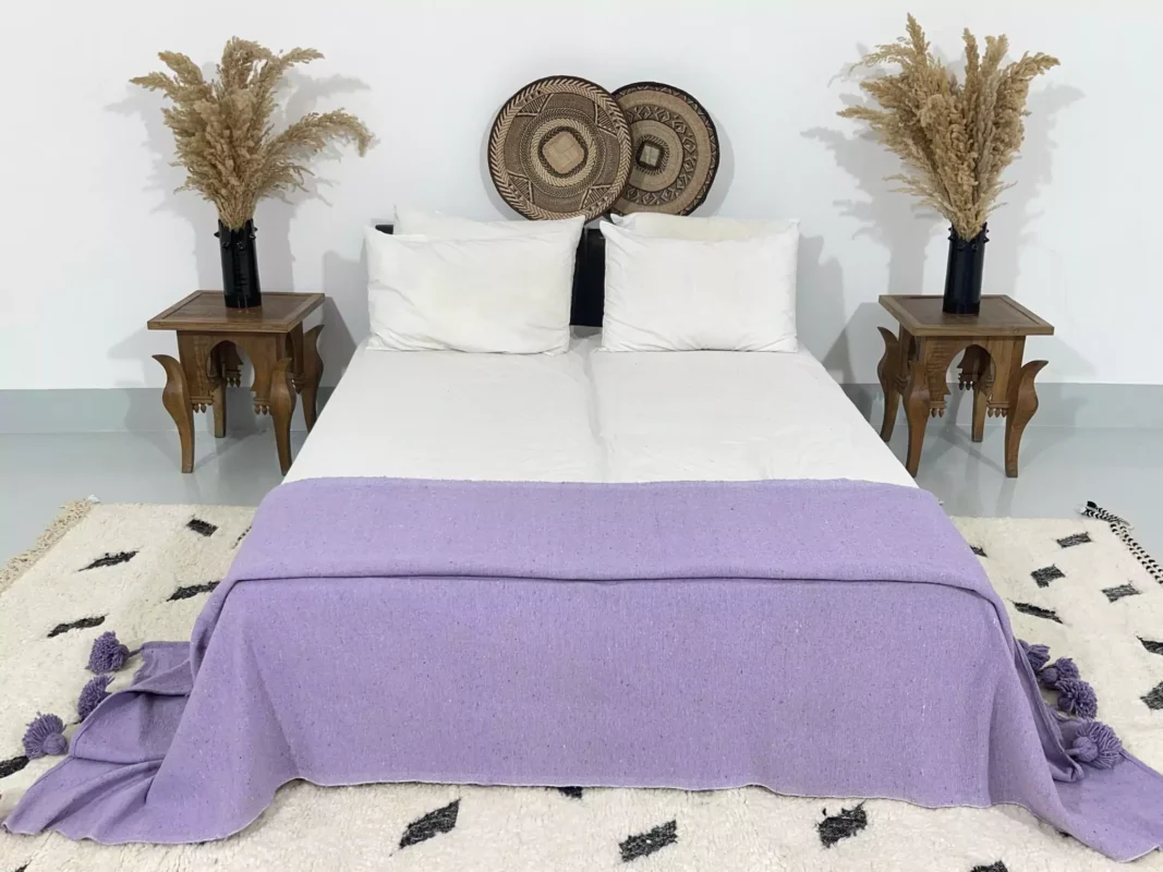 Purple pompom blanket folded across the lower half of a white bed