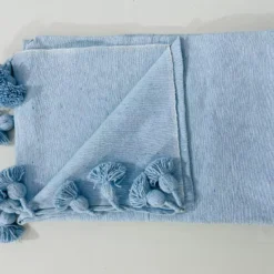 Baby blue cotton blanket lit by natural sunlight in soft neutral room