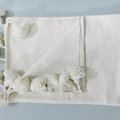 White cotton throw blanket draped over a neutral-toned modern sofa