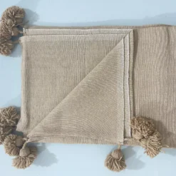 Soft beige Moroccan blanket with pompoms styled on a cozy sofa