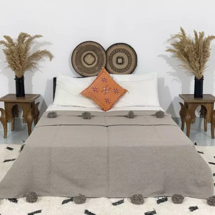 Handmade Moroccan pompom blanket in taupe color on a bed