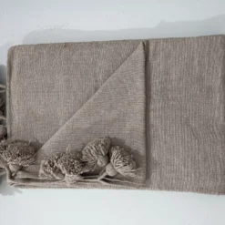 Taupe pompom blanket casually draped over a wooden chair