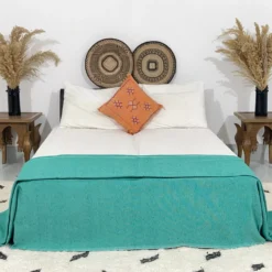 Teal Moroccan pompom blanket styled in a boho bedroom with neutral tones