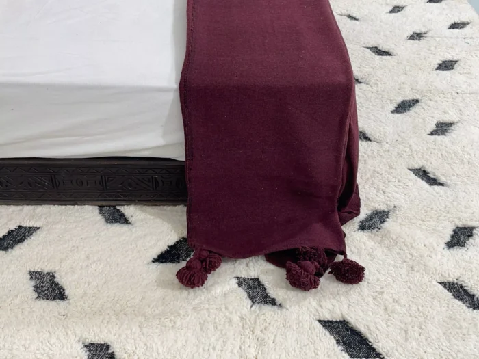 Burgundy cotton throw blanket illuminated by soft natural light
