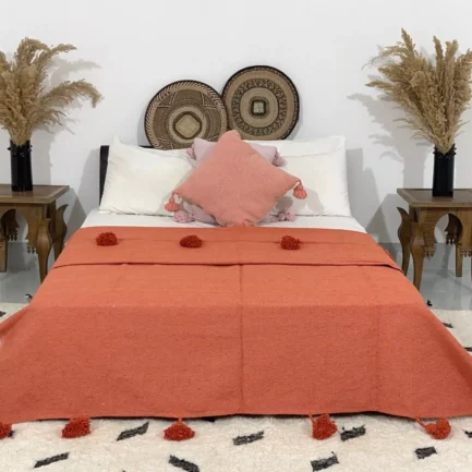Handmade terracotta Moroccan cotton pompom blanket styled on a bed