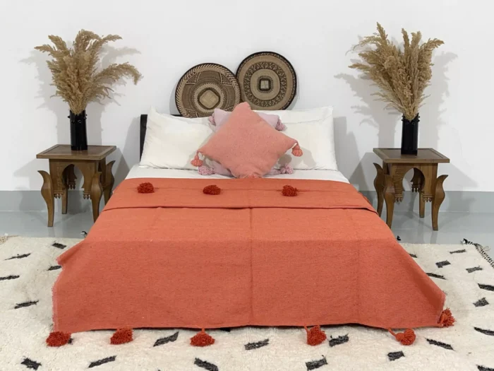 Handmade terracotta Moroccan cotton pompom blanket styled on a bed