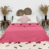 Handmade Moroccan pompom blanket in rose pink displayed on a bed