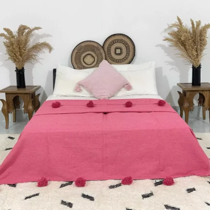 Handmade Moroccan pompom blanket in rose pink displayed on a bed