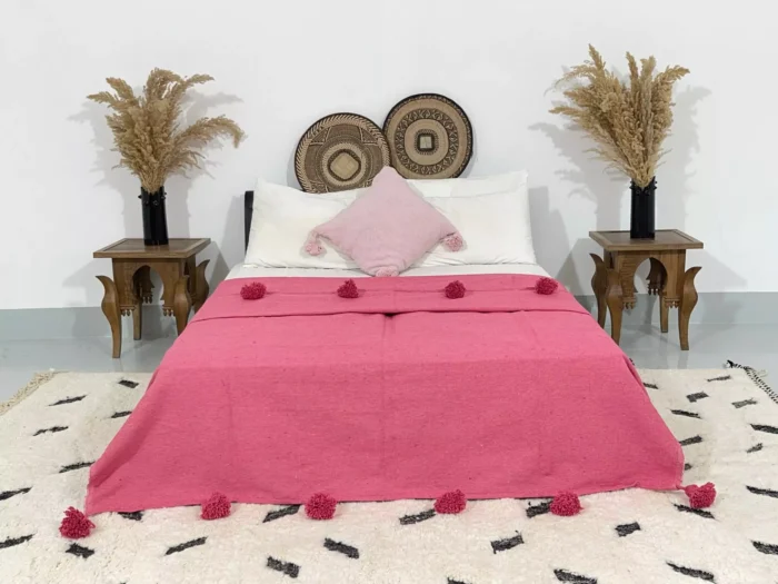 Handmade Moroccan pompom blanket in rose pink displayed on a bed