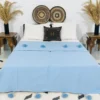 Handmade baby blue Moroccan pompom blanket displayed on a modern bed