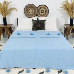 Handmade baby blue Moroccan pompom blanket displayed on a modern bed